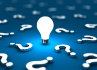 faq-questions Lightbulb in center of blue table surrounded by question marks